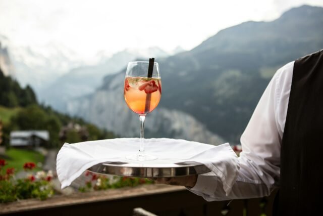 Waiter holding cocktail with mountain scenery in the background.
