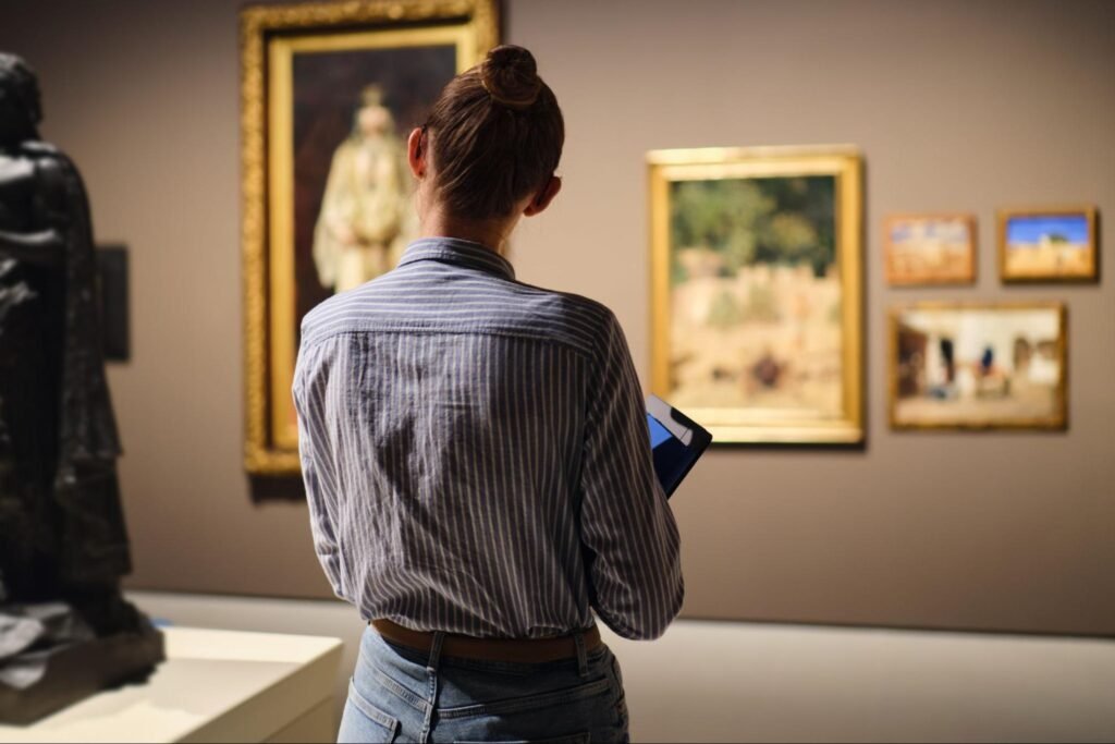 A person standing in an art museum viewing framed paintings on the wall.
